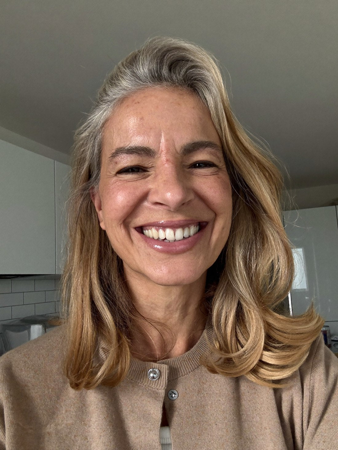 Selfie von Sabine, Anfang 50, strahlende pralle Haut und volles Haar, lächelt in ihrer Küche