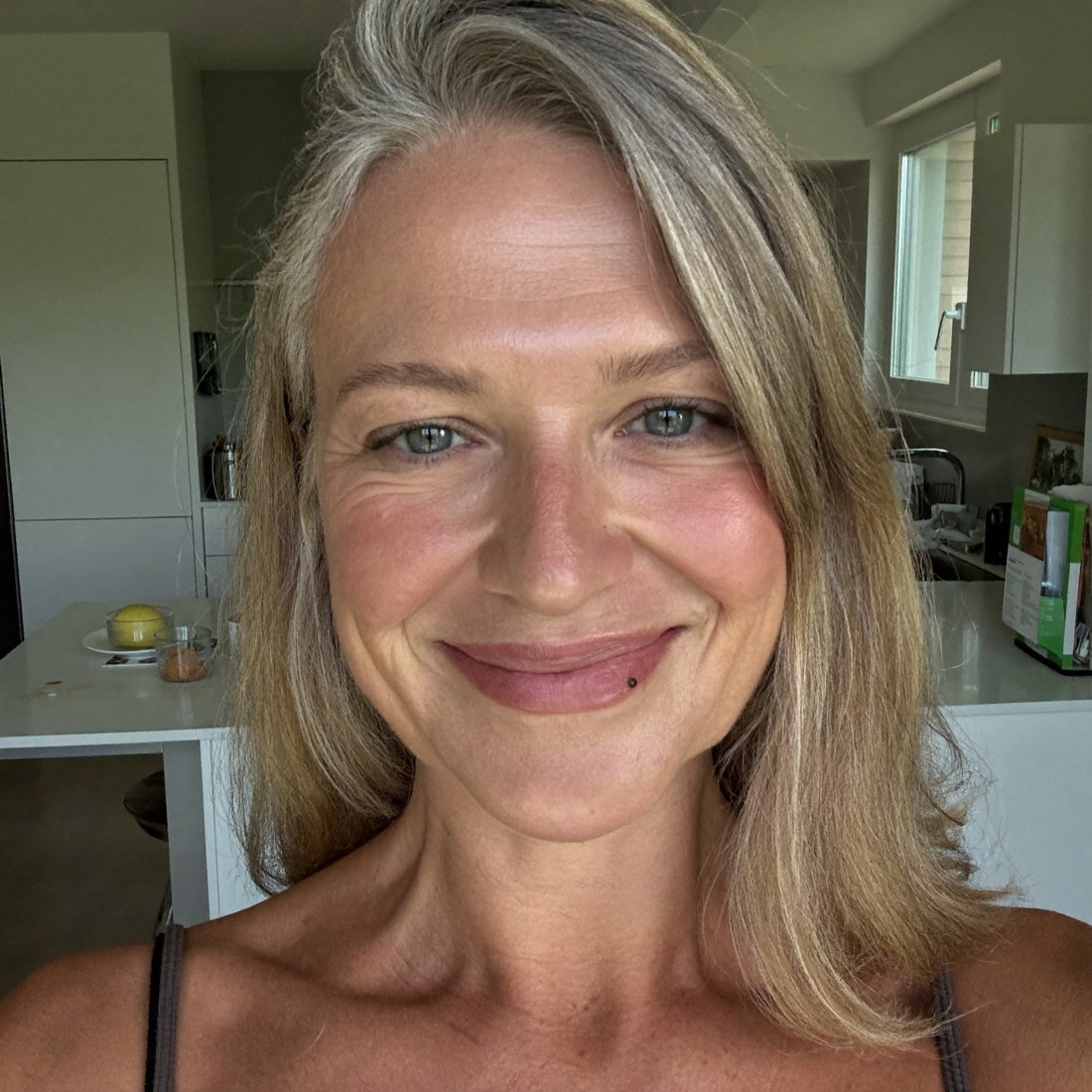 Selfie van Ingrid, begin 50, stralende, volle huid en vol haar, lacht in haar keuken