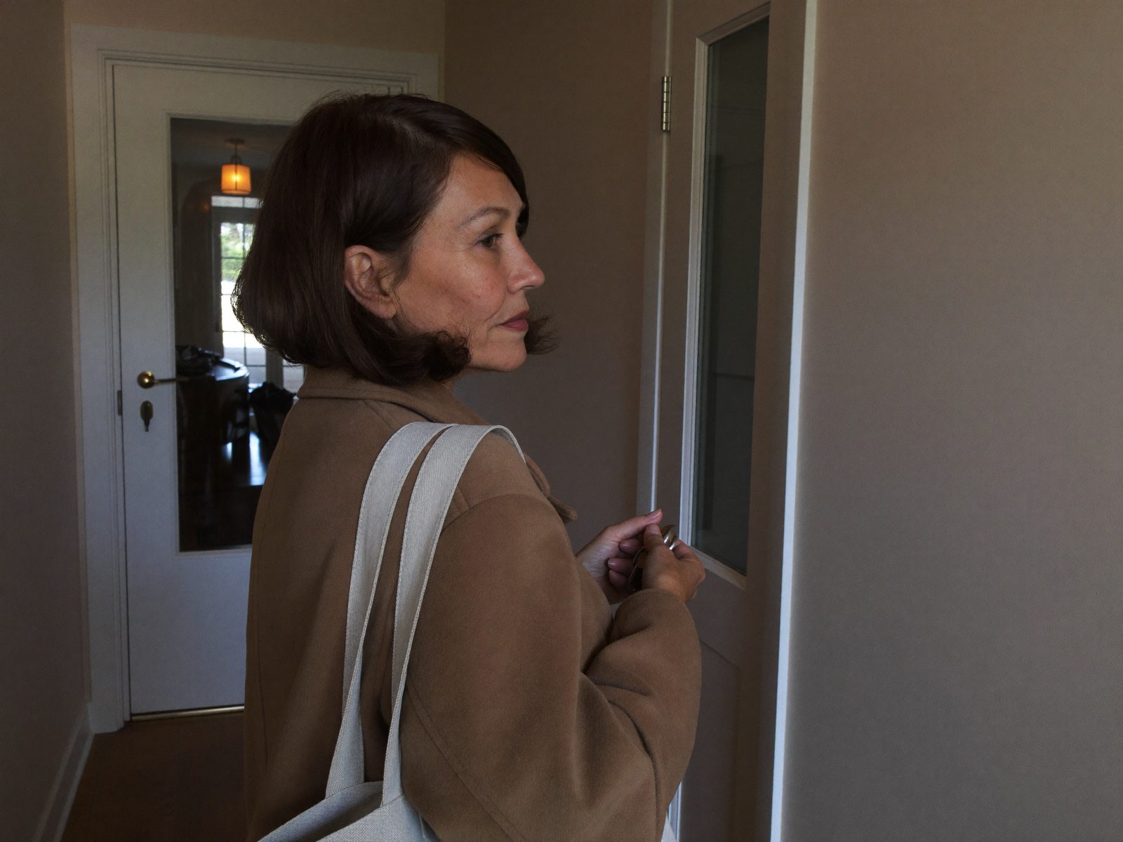 Donna con il cappotto nell'ingresso la mattina presto che guarda verso la porta di casa, pronta a uscire